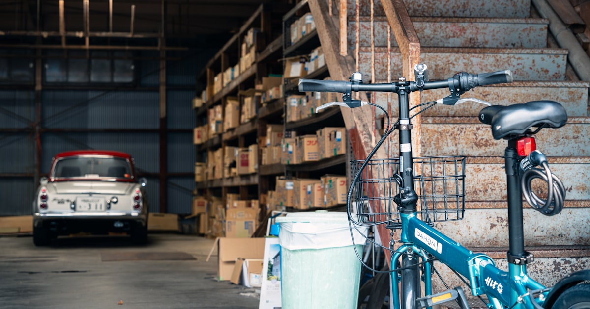 Bicycle parked in a cluttered warehouse with a vintage car.
