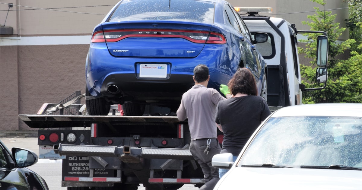 A blue car being loaded onto a flatbed truck