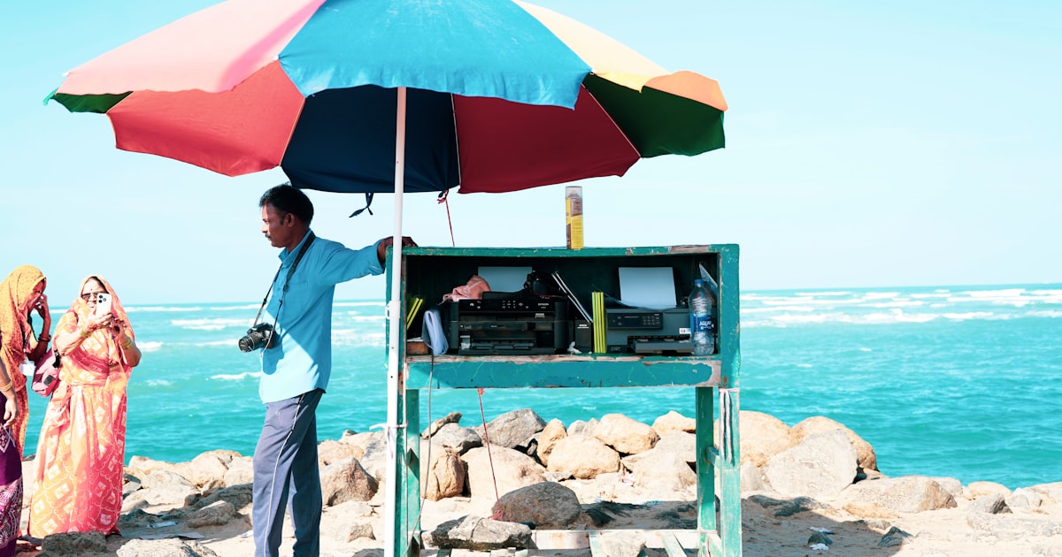 Man stands by a typewriter stand under a colorful umbrella.
