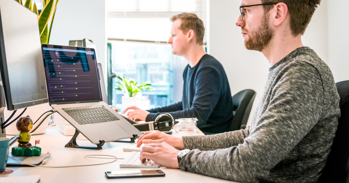 Man sitting on chair wearing gray crew-neck long-sleeved shirt using apple magic keyboard