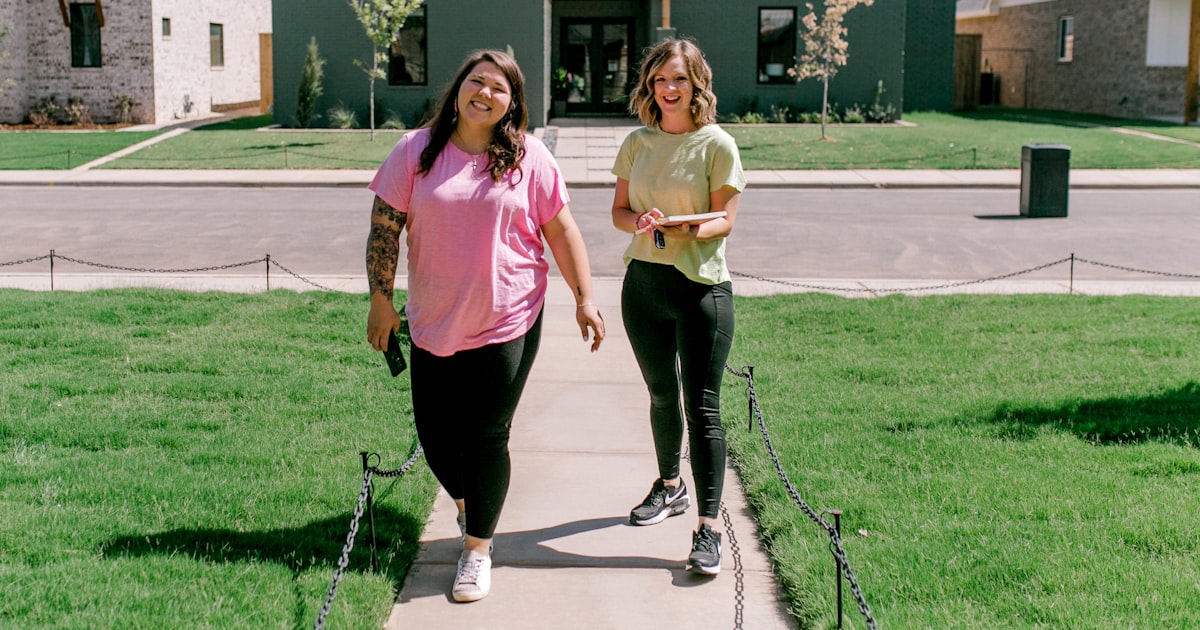Two smiling women walk towards a modern green house.