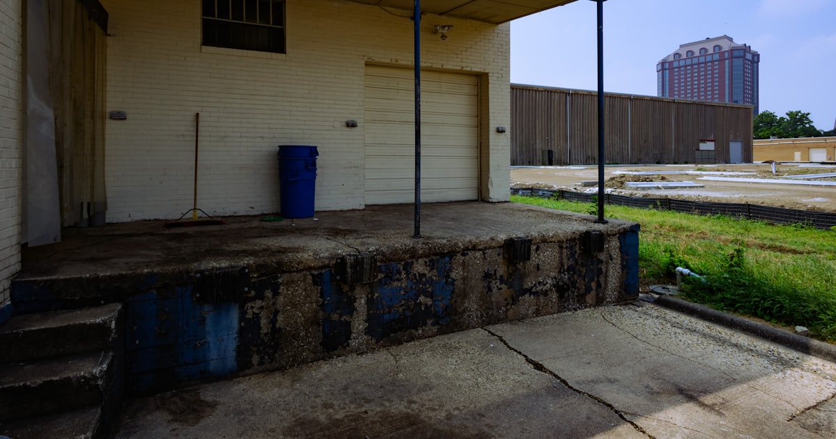 a white building with a blue trash can in front of it