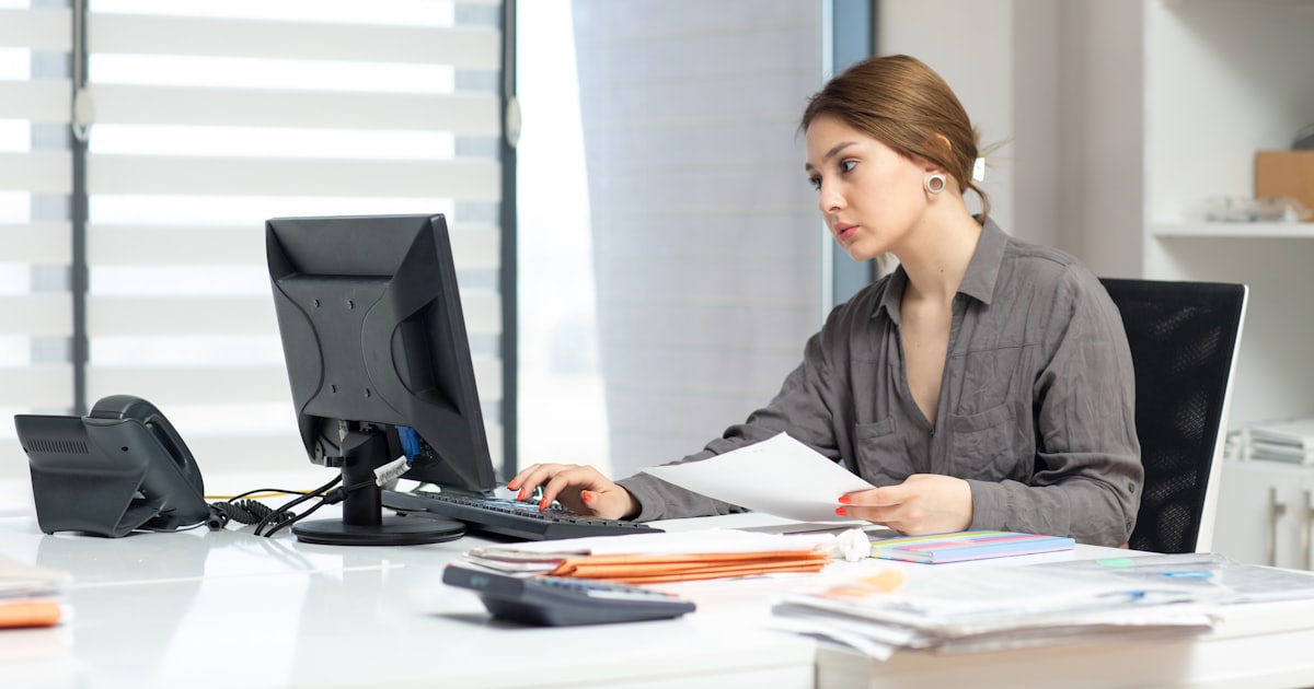 Young woman focused on a computer and documents at an office desk