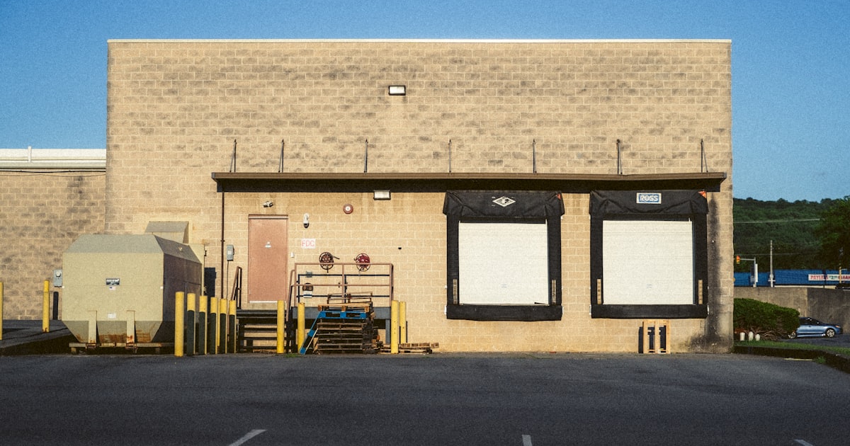 A beige concrete warehouse building with two loading docks and a dumpster