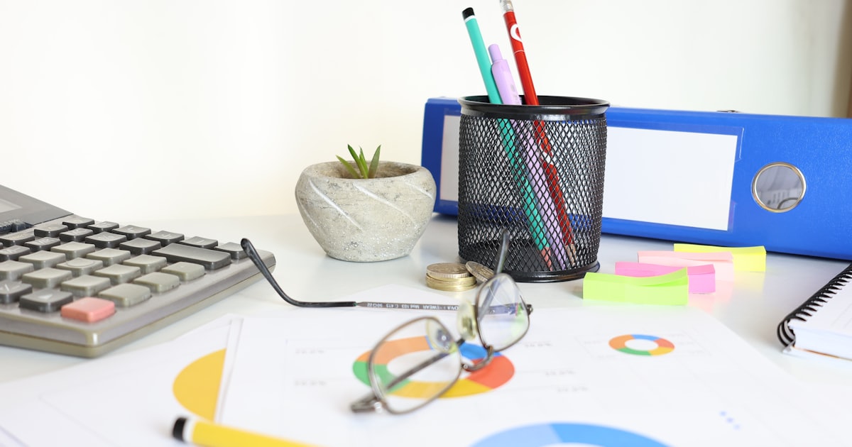 Desk with calculator, glasses, charts and office supplies