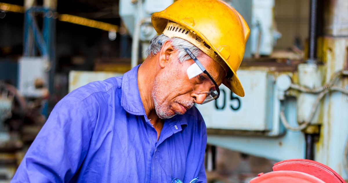 man grinding a metal tool on industrial machinery