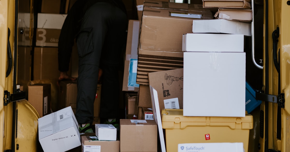 A person in dark clothing loading cardboard boxes into a yellow delivery van