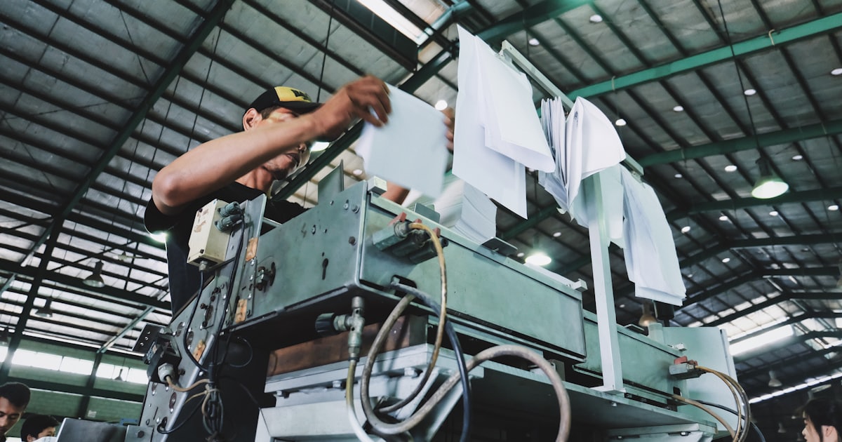 man holding papers while operating a large grey industrial machine