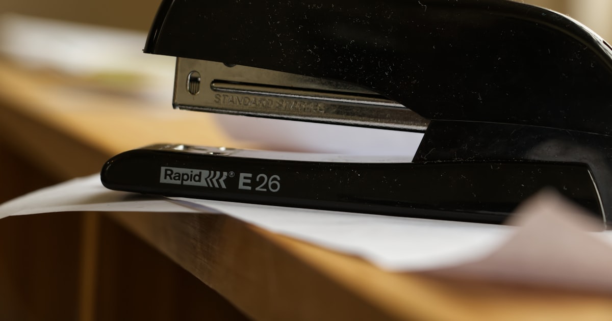 A black stapler rests on a desk with papers