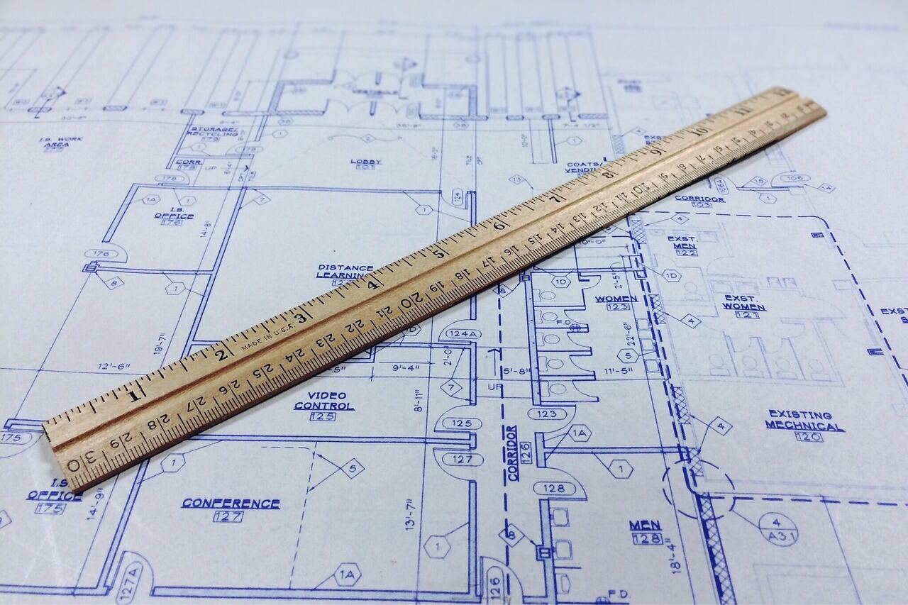 A wooden scale ruler laid across a blueprint floor plan