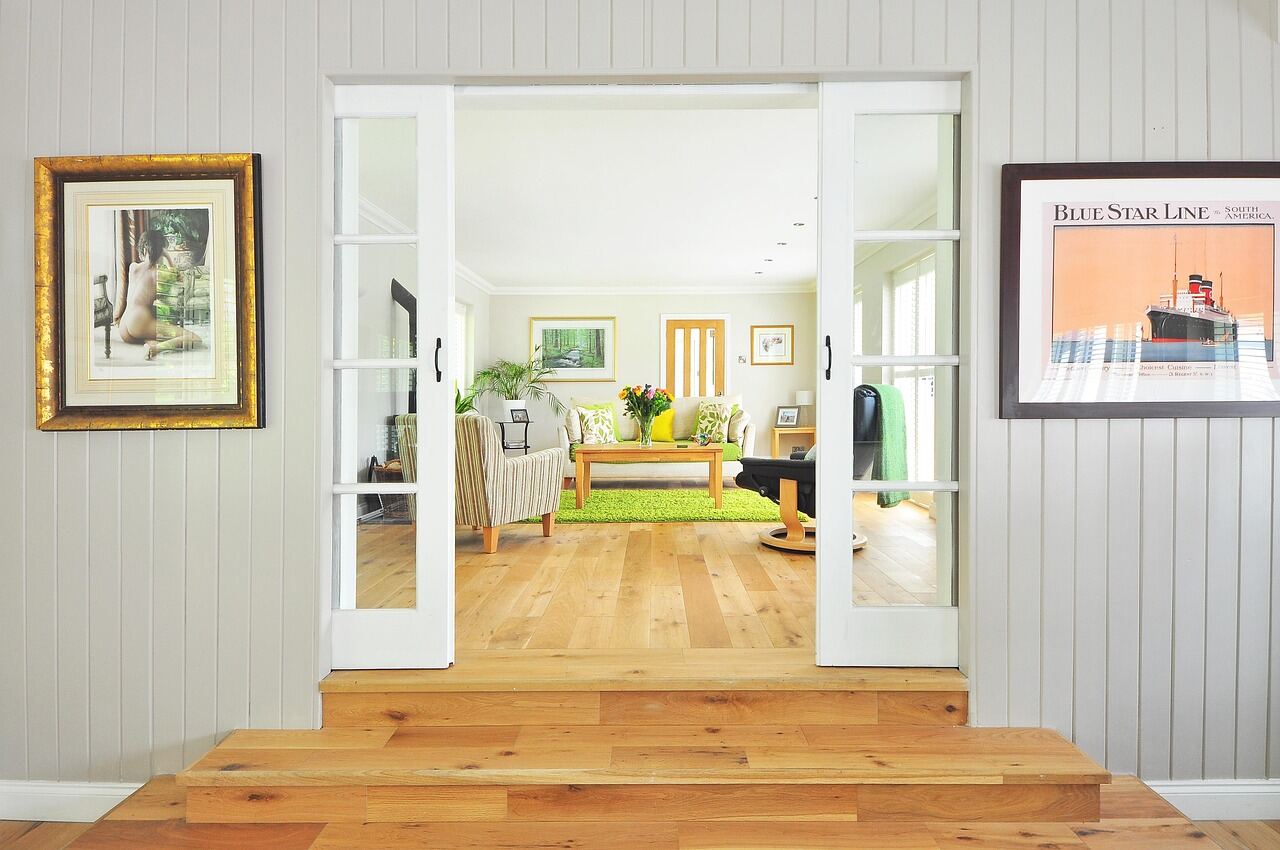 A bright, minimally furnished living room seen through open French doors, wood flooring throughout