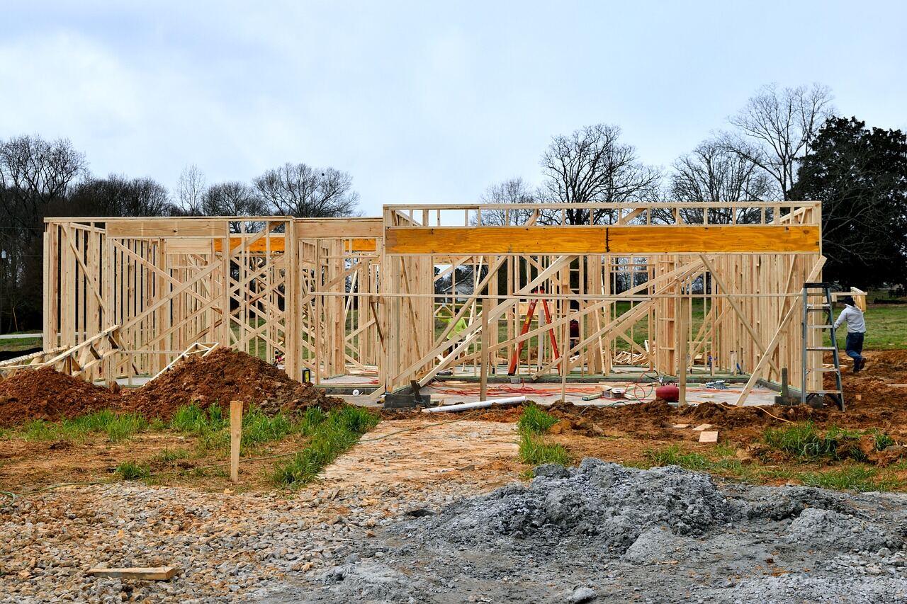 A wood-framed house under construction, structural framing exposed against the sky