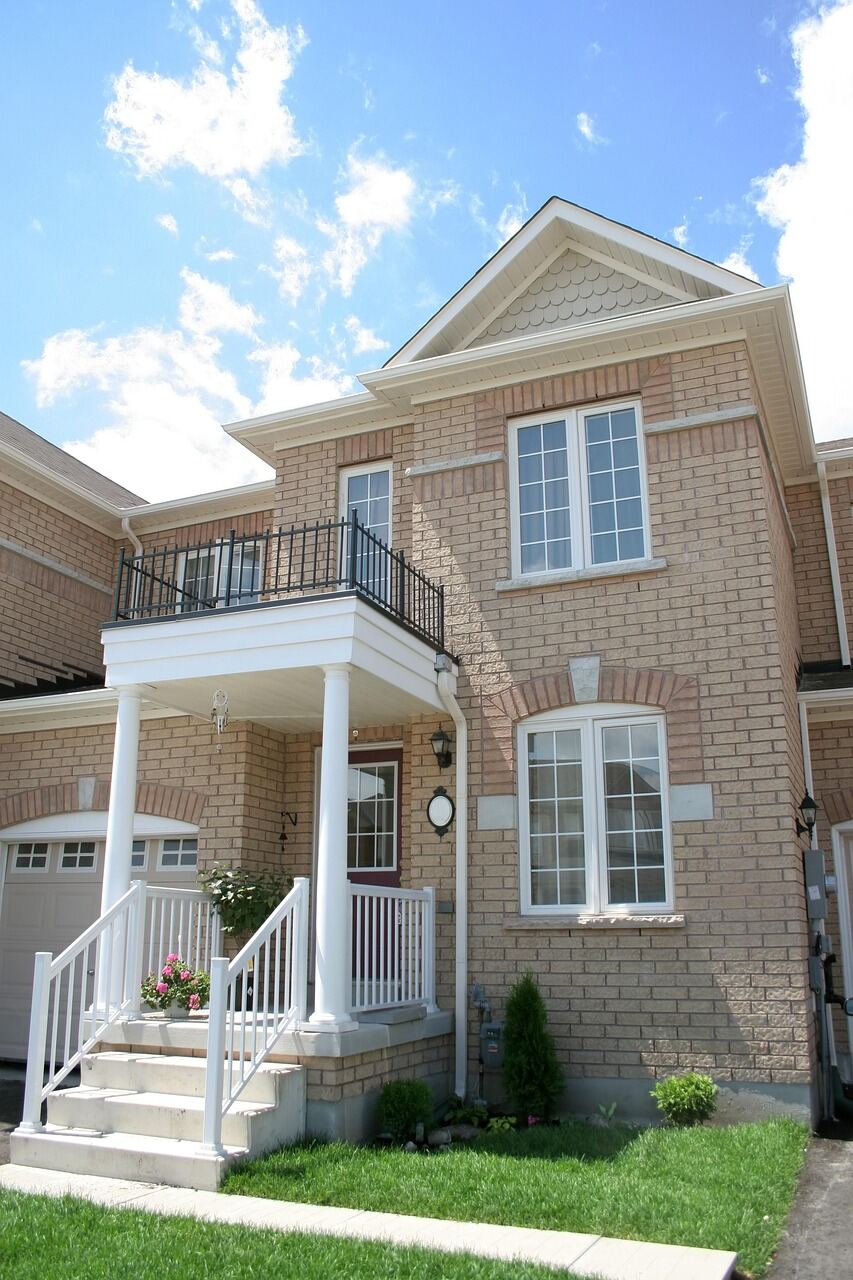 A two-storey brick duplex with a covered upper balcony and ground-floor garage, on a narrow urban infill lot