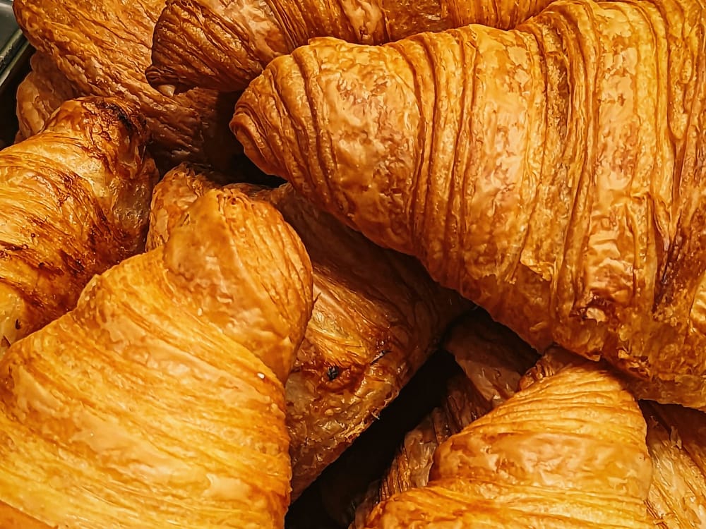 Fresh butter croissants stacked on a white marble slab, shatteringly flaky