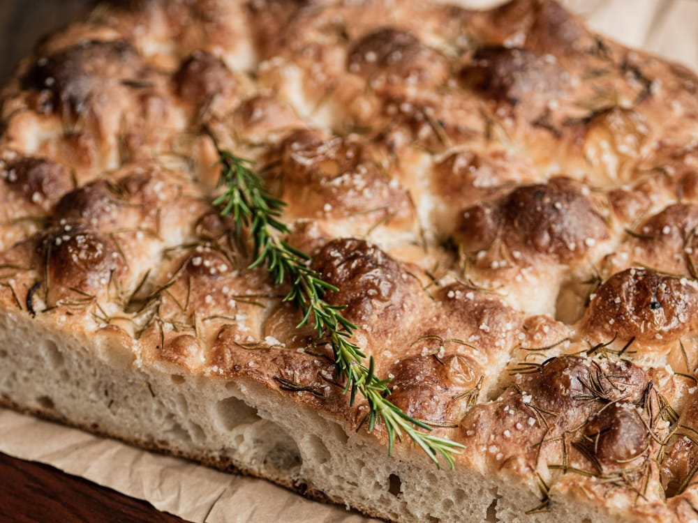 Rows of focaccia with rosemary and sea salt, golden on a sheet pan
