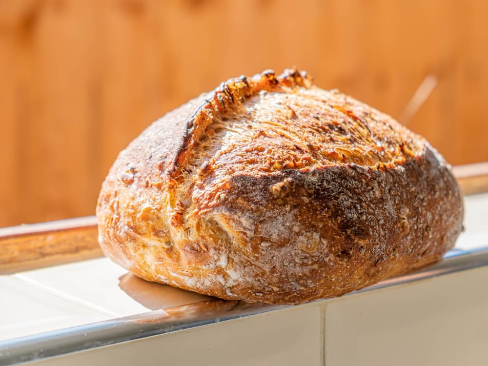 A rustic sourdough country loaf with scored wheat pattern, golden crust, on a wooden board