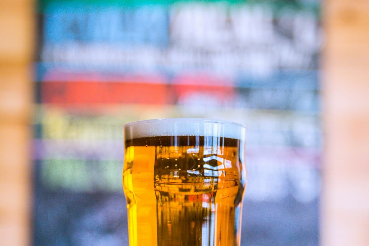 A close-up of a clear amber pint of Copper Ridge IPA held up to industrial light, beer glowing golden