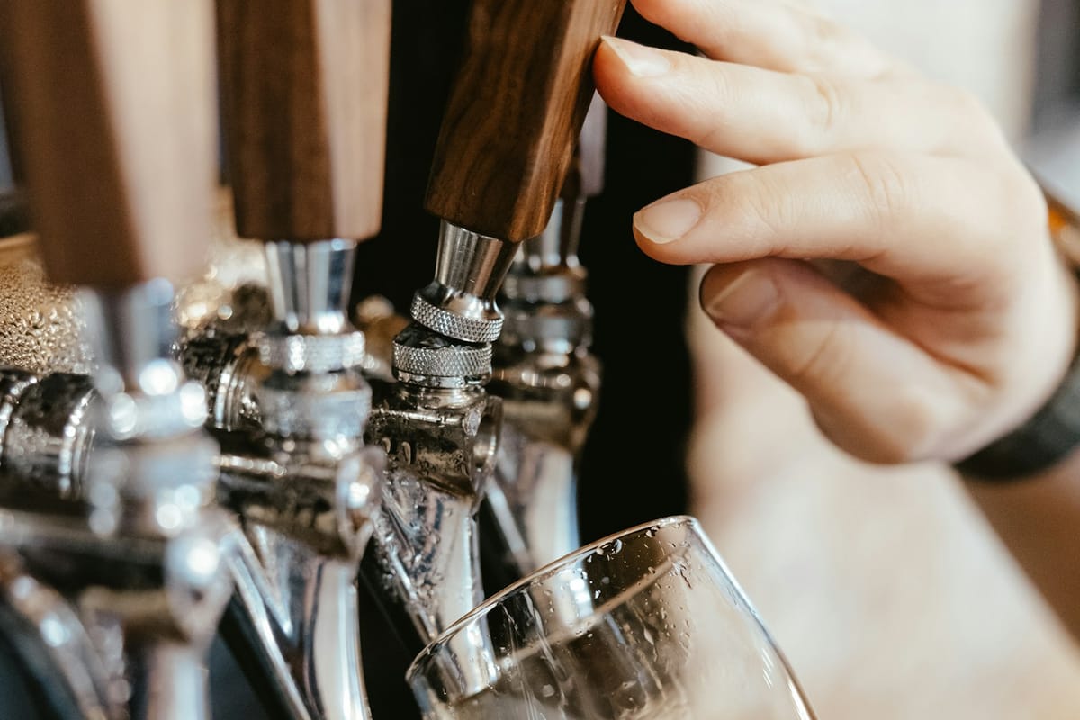 Craft beer pouring from the tap with a clean white head forming, bar top visible below