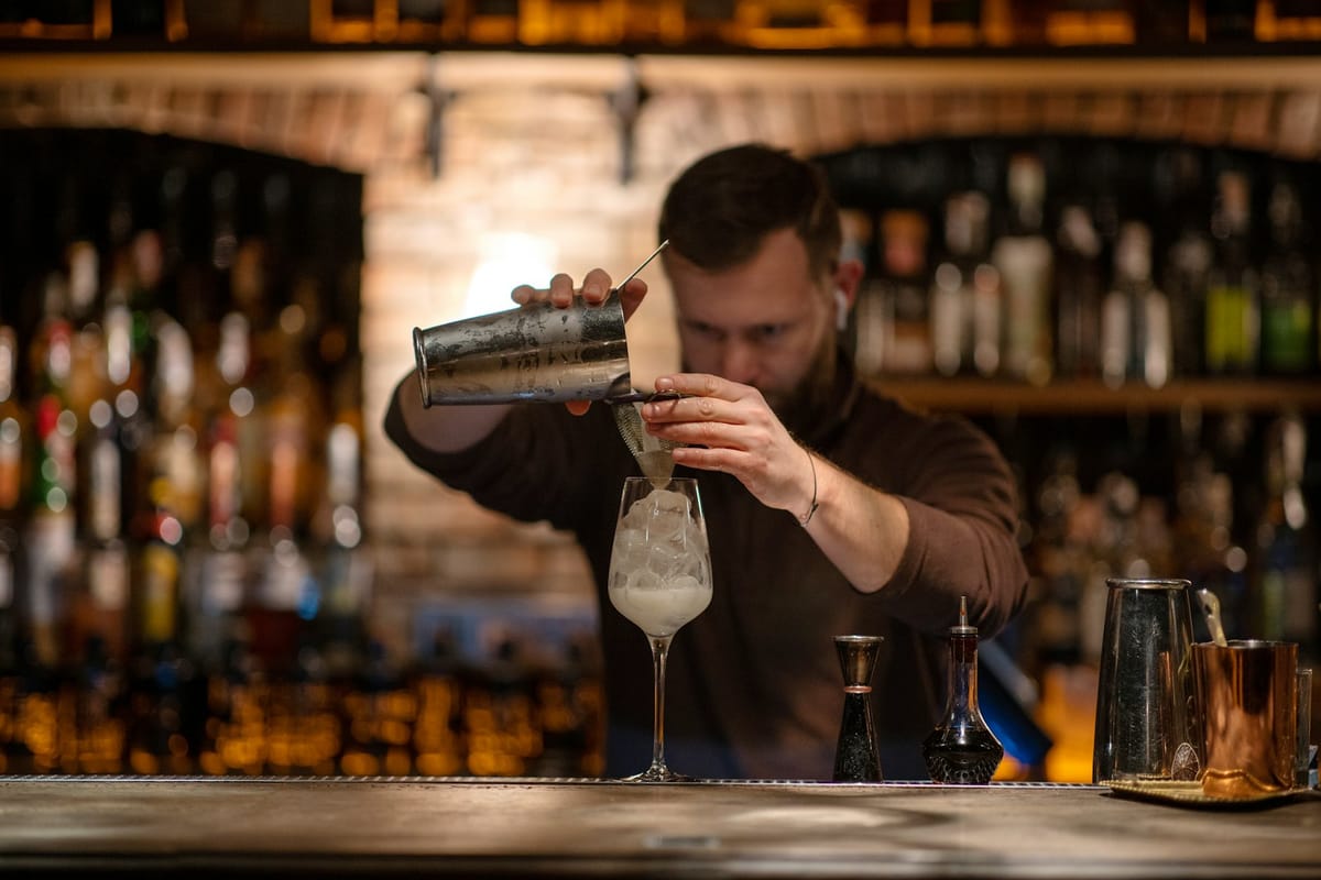 A bartender mid-stir, barspoon in a crystal mixing glass, low light behind the bar