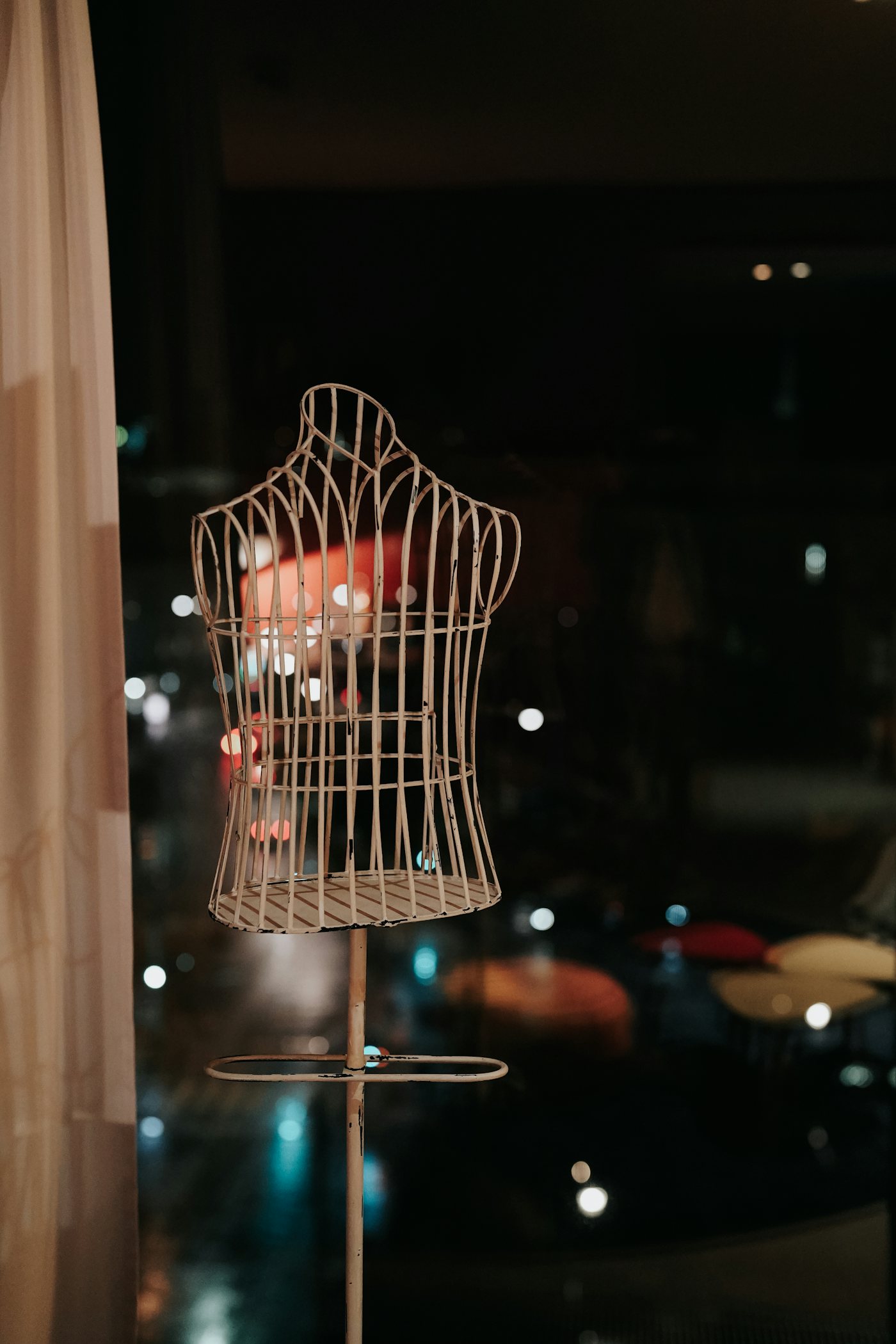 A decorative wire dress form on a stand, silhouetted against a dim, atmospheric room