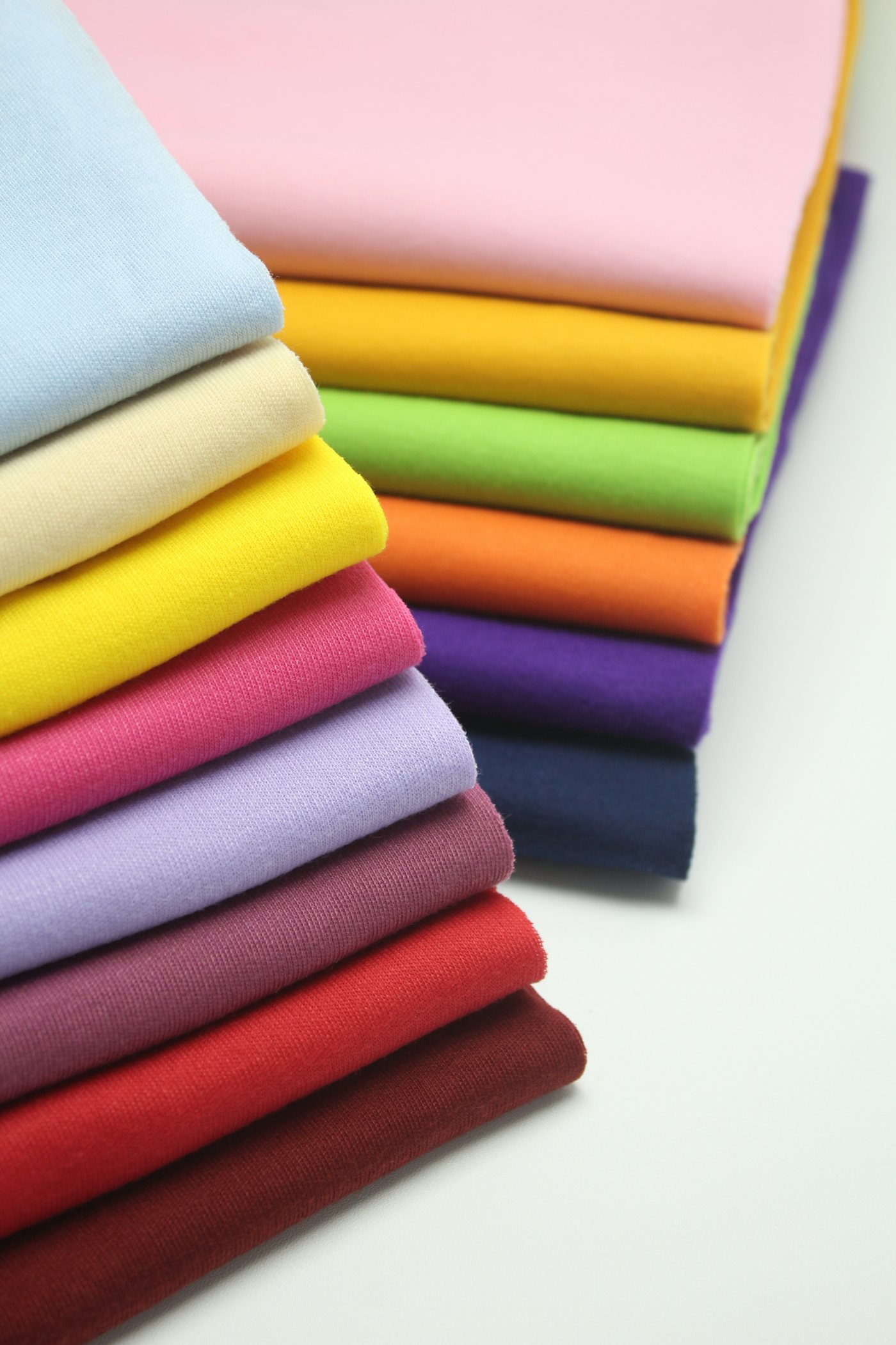 A stack of folded fabric in a dozen different colours, viewed close up