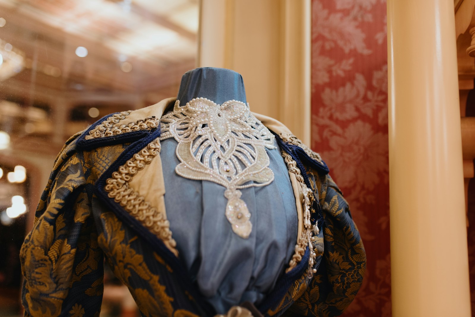 A close-up of an ornate blue and gold beaded opera bodice displayed on a dress form