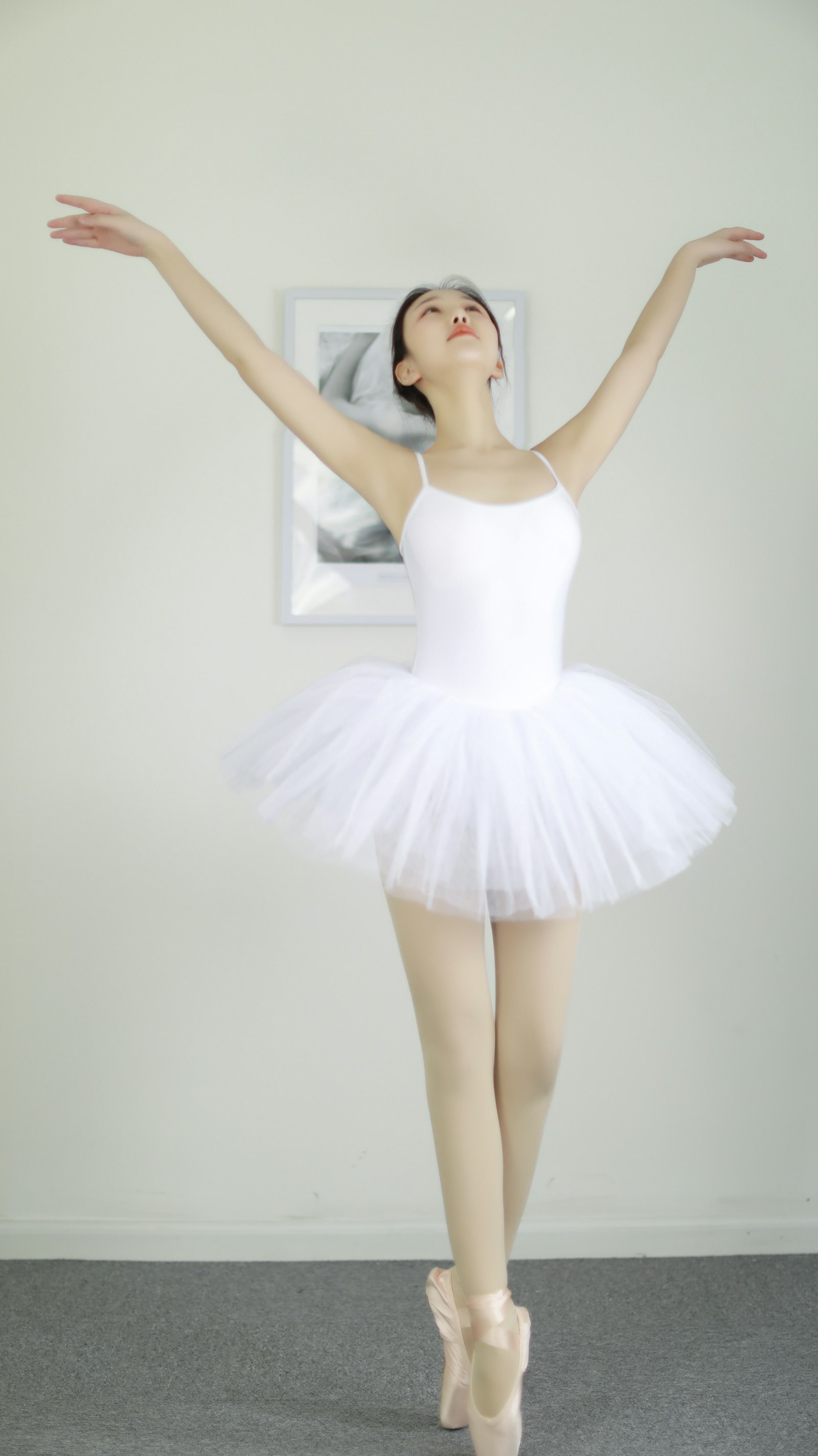 A ballet dancer in a white tutu and pointe shoes, arms raised in a classical pose