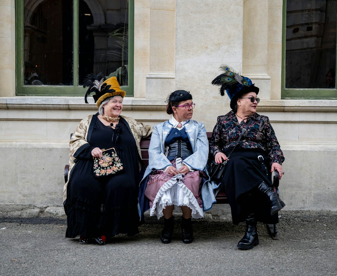 Three performers seated together in elaborate late-Victorian-era hats and formal dress