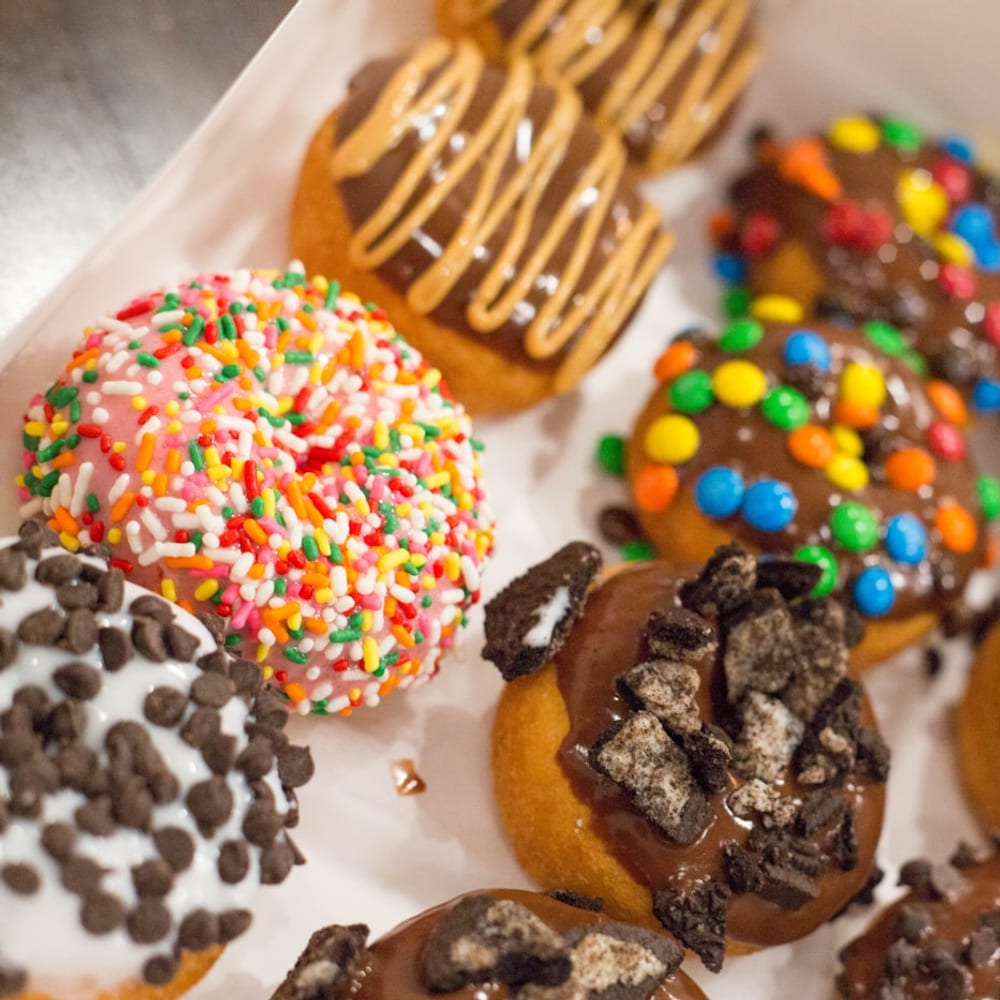An open dozen box filled with a colourful mix of glazed, filled, and cake donuts