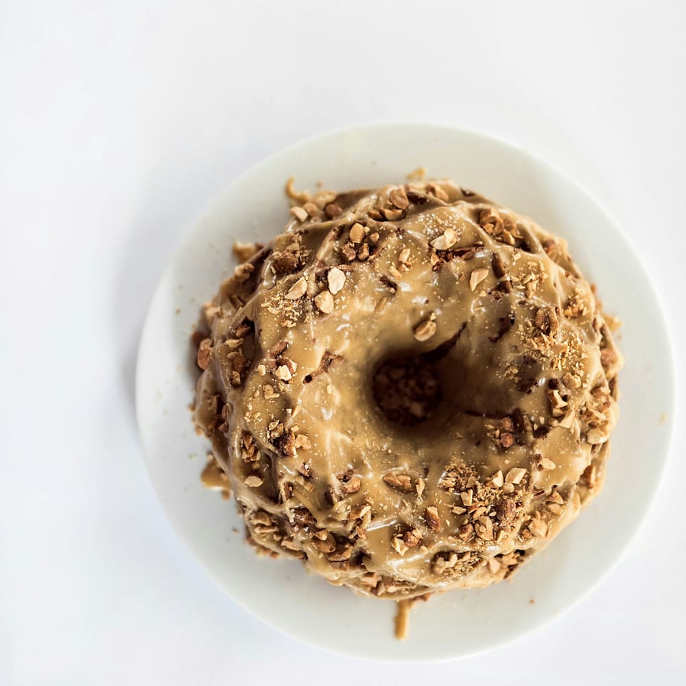 A maple bacon twist donut on kraft paper with candied bacon crumble scattered around it