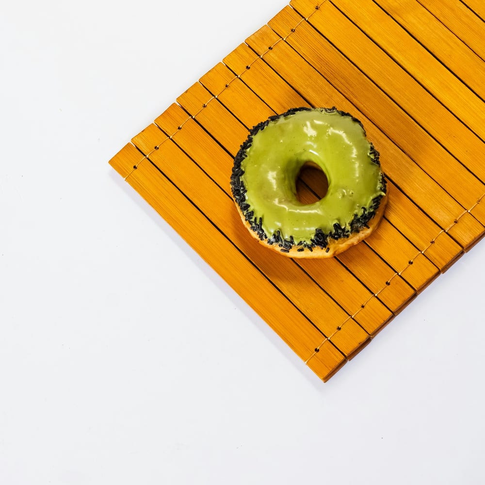 Close-up of a matcha coconut donut with toasted coconut flakes on a green-glazed ring