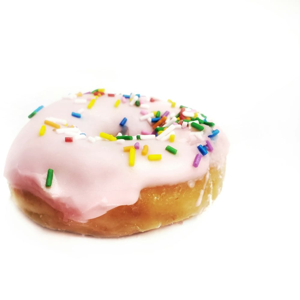 A tray of strawberry-glazed donuts topped with rainbow sprinkles on a white marble counter