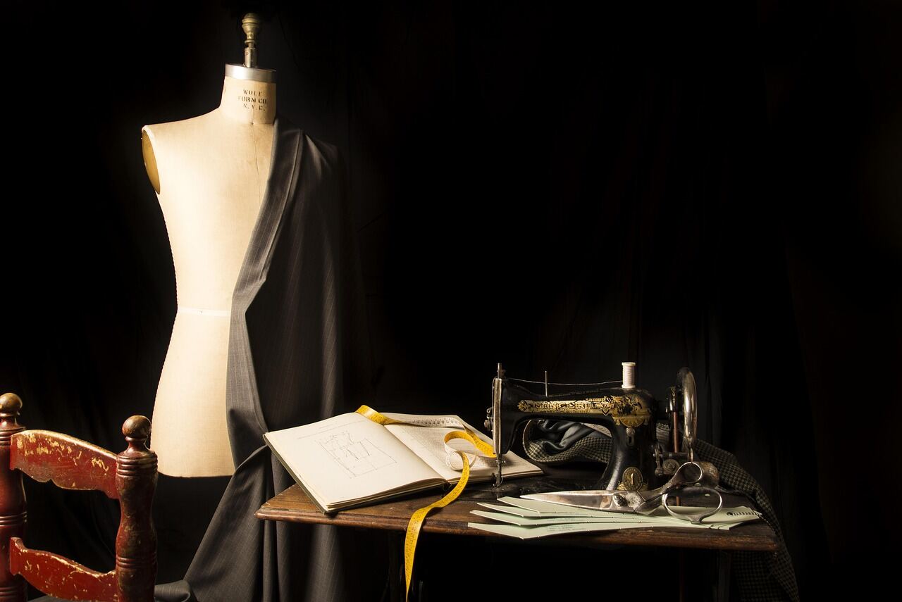 A tailor's worktable covered in pinned fabric and a paper pattern, mid cut