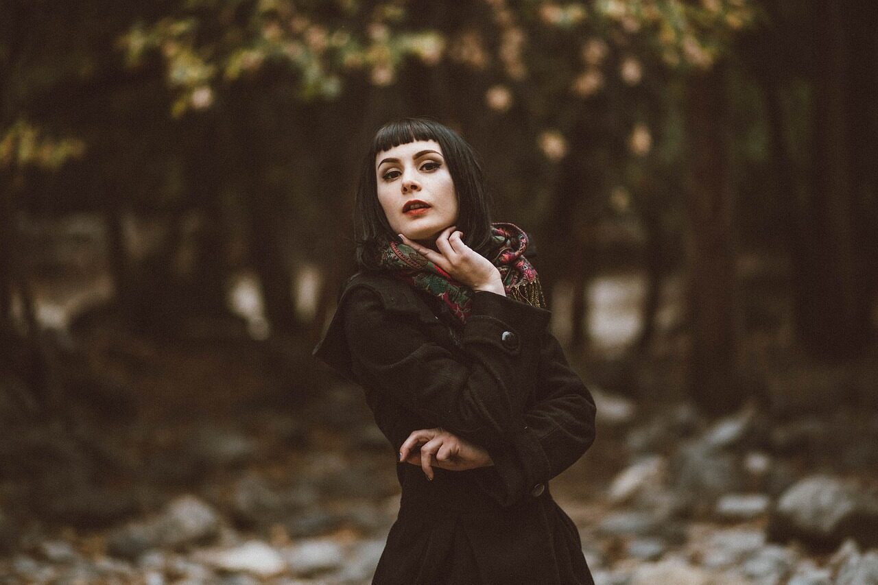 A woman in a dark high-collared coat photographed against autumn foliage
