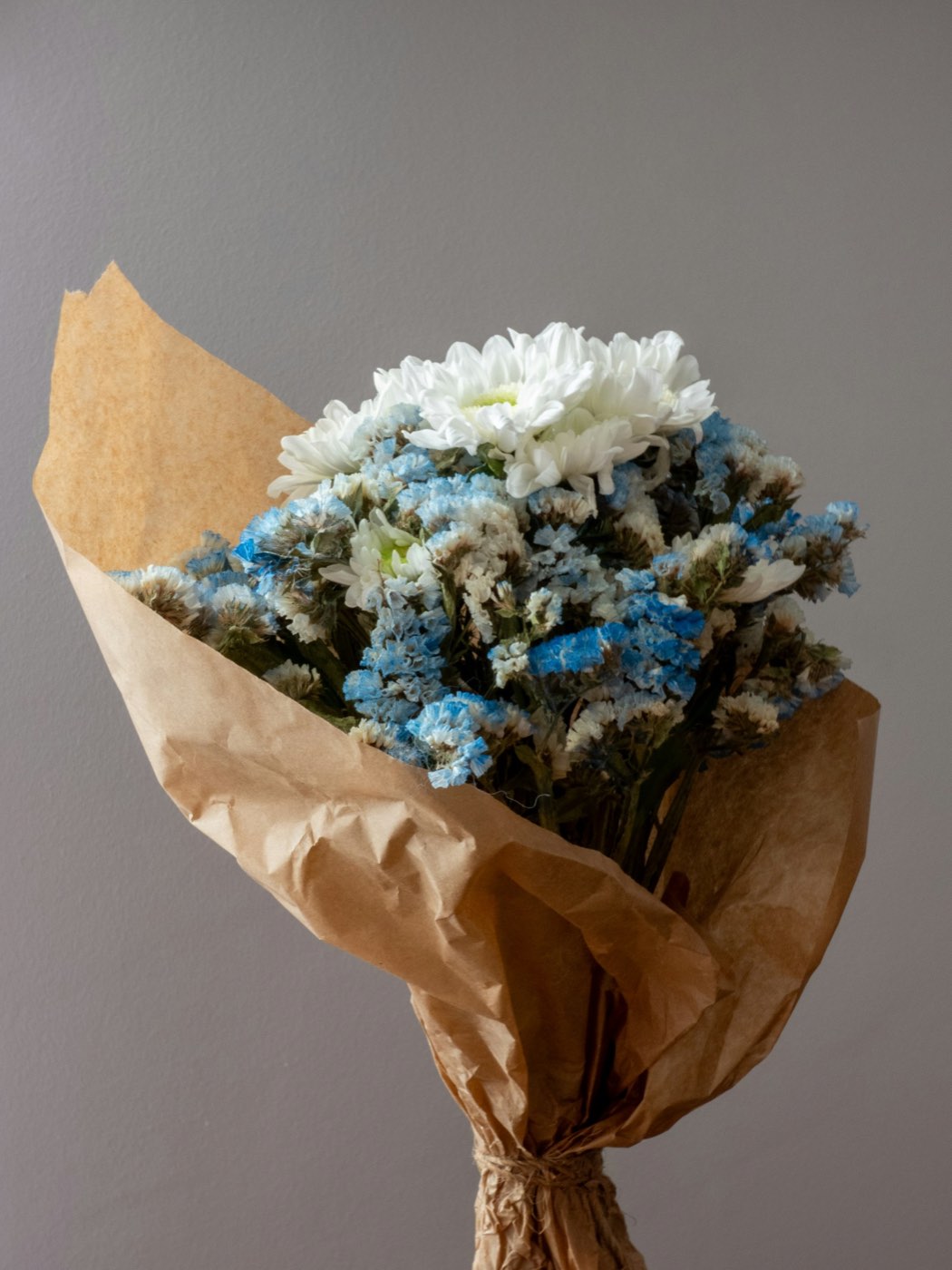 White chrysanthemums and blue statice wrapped in kraft paper, tied with twine