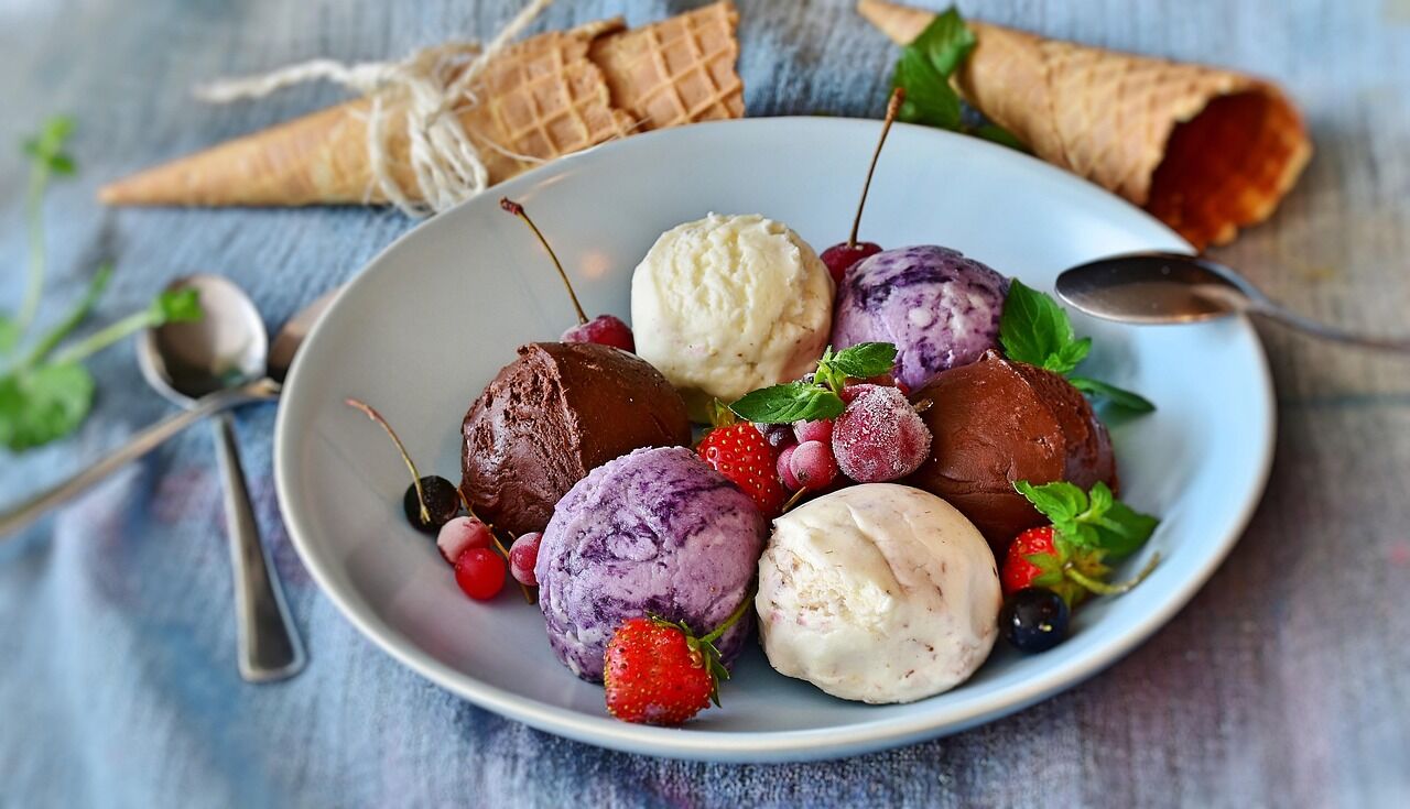 Scoops of vanilla, chocolate and berry gelato in a white bowl with fresh berries and cherries
