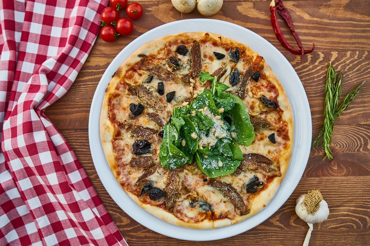 A whole pizza topped with spinach and olives on a white plate over a red gingham cloth