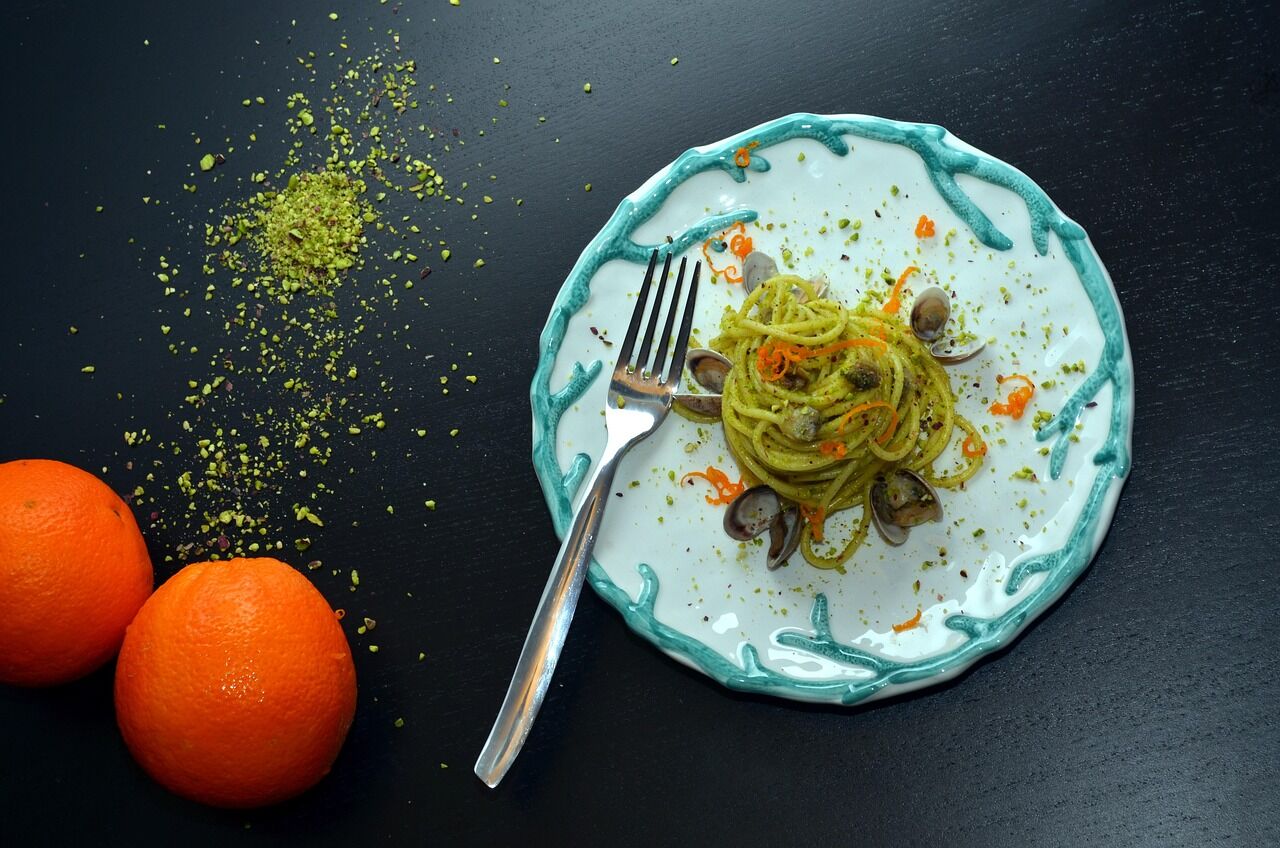 A nest of green linguine on a turquoise plate with a fork, shot from above on dark slate