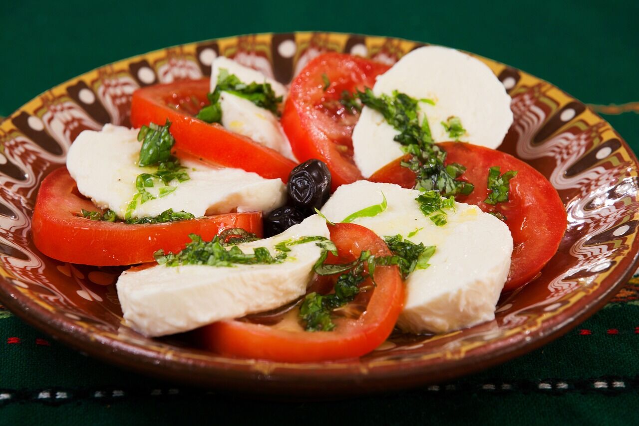Sliced tomato and mozzarella dressed with pesto on a wooden platter