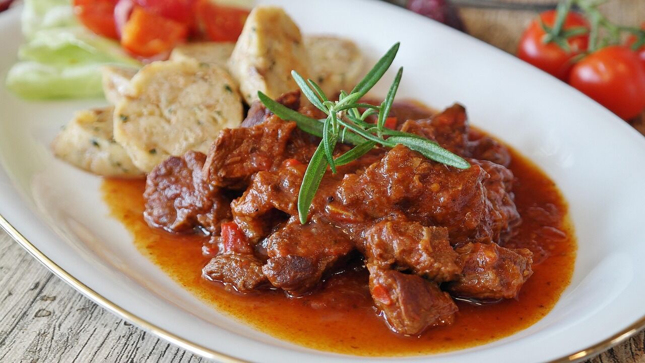 Beef goulash in a dark sauce with bread dumplings and a sprig of rosemary