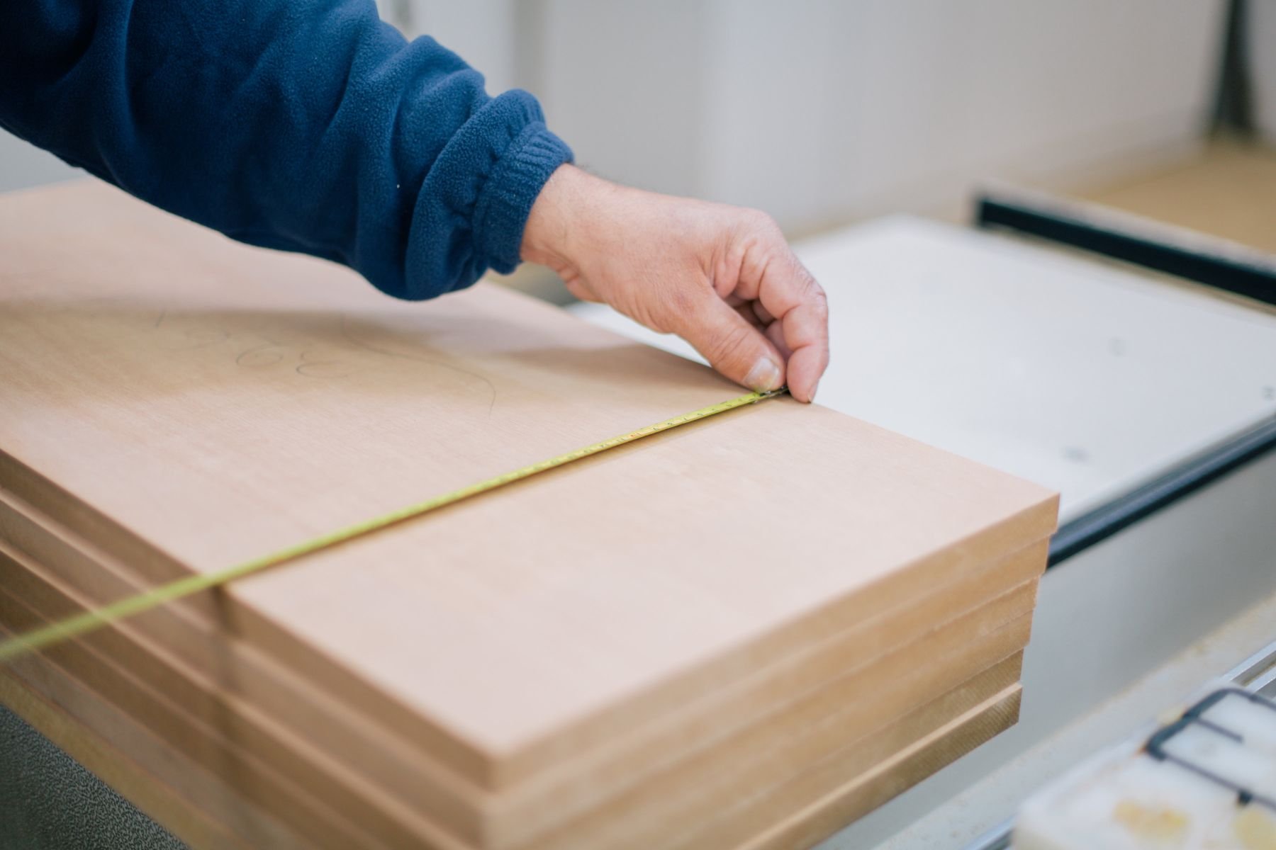A hand running a tape measure along the edge of a stack of milled boards
