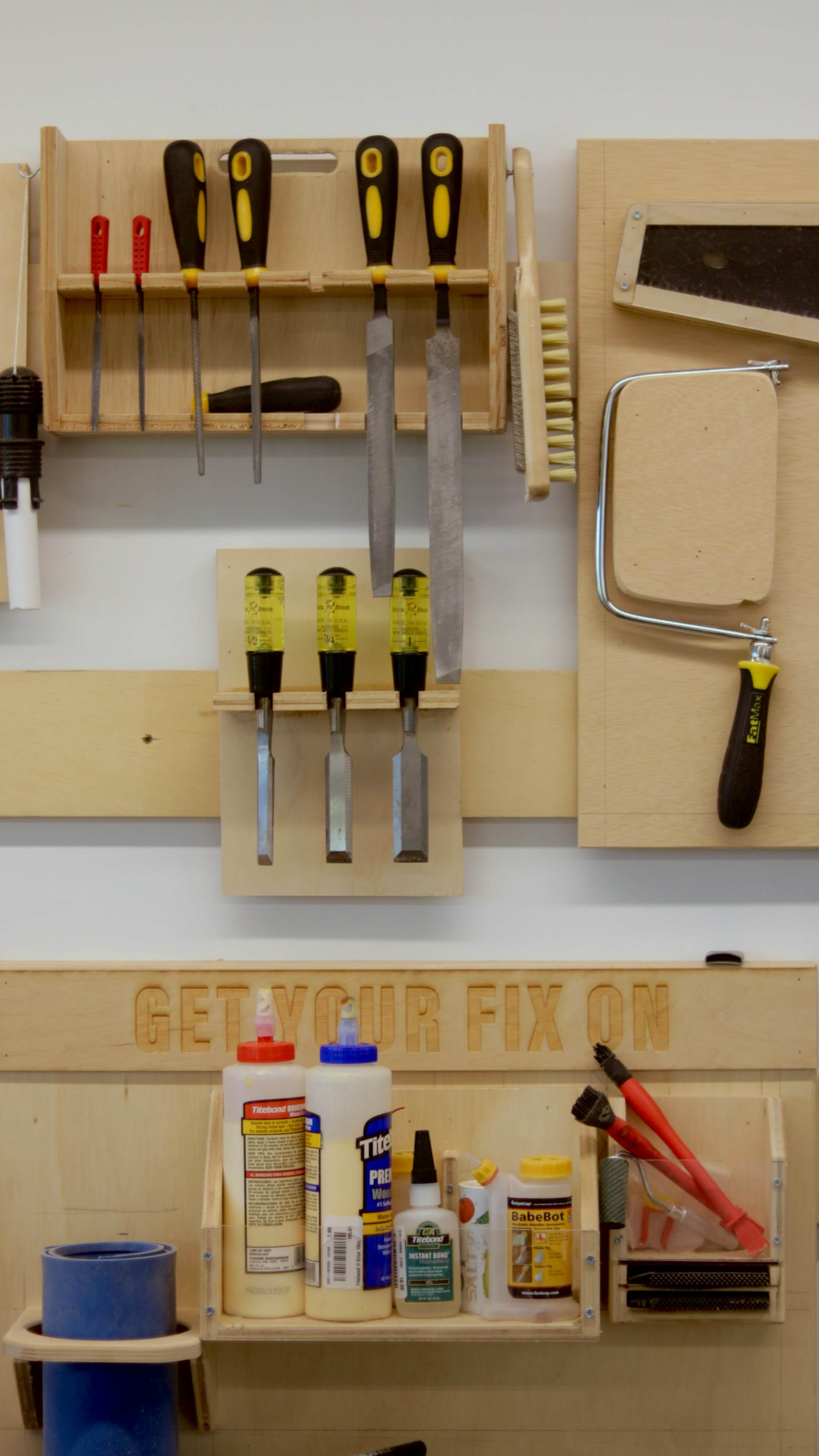 A shop wall holding files, chisels and glue within reach of the bench