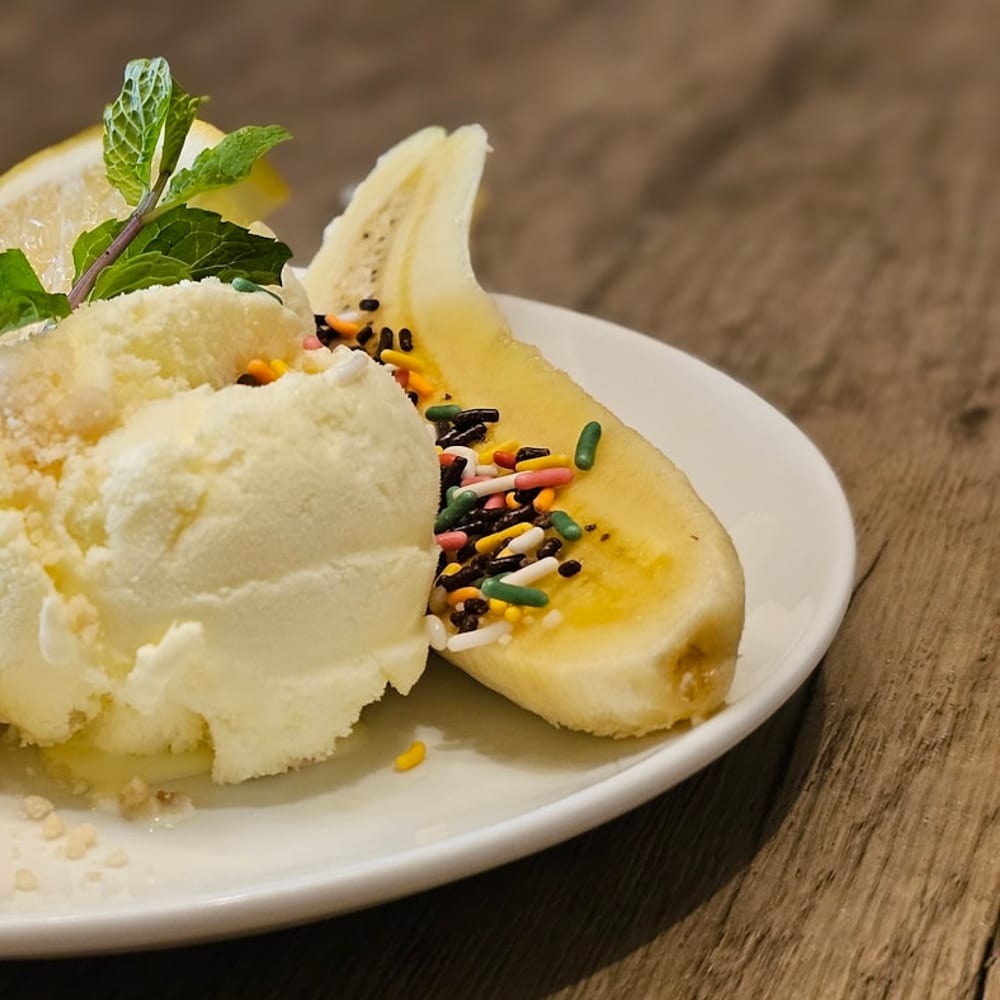 A banana split sundae with three scoops, hot fudge, and toasted walnuts served in a long white dish