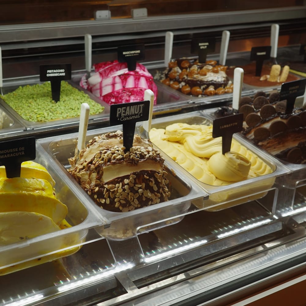 A row of gelato pans in pistachio green, strawberry red, and vanilla cream inside the gelateria case
