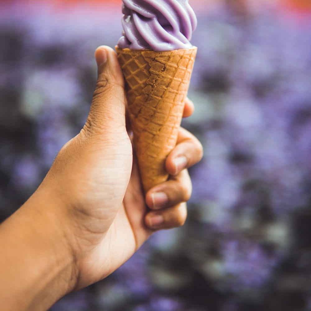 A cone of honey lavender gelato with a golden honeycomb garnish, held against a bright Austin sky