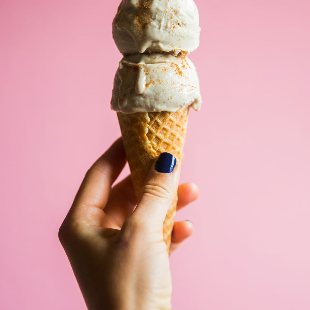 Three stacked scoops of pistachio, strawberry, and vanilla gelato in a homemade waffle cone