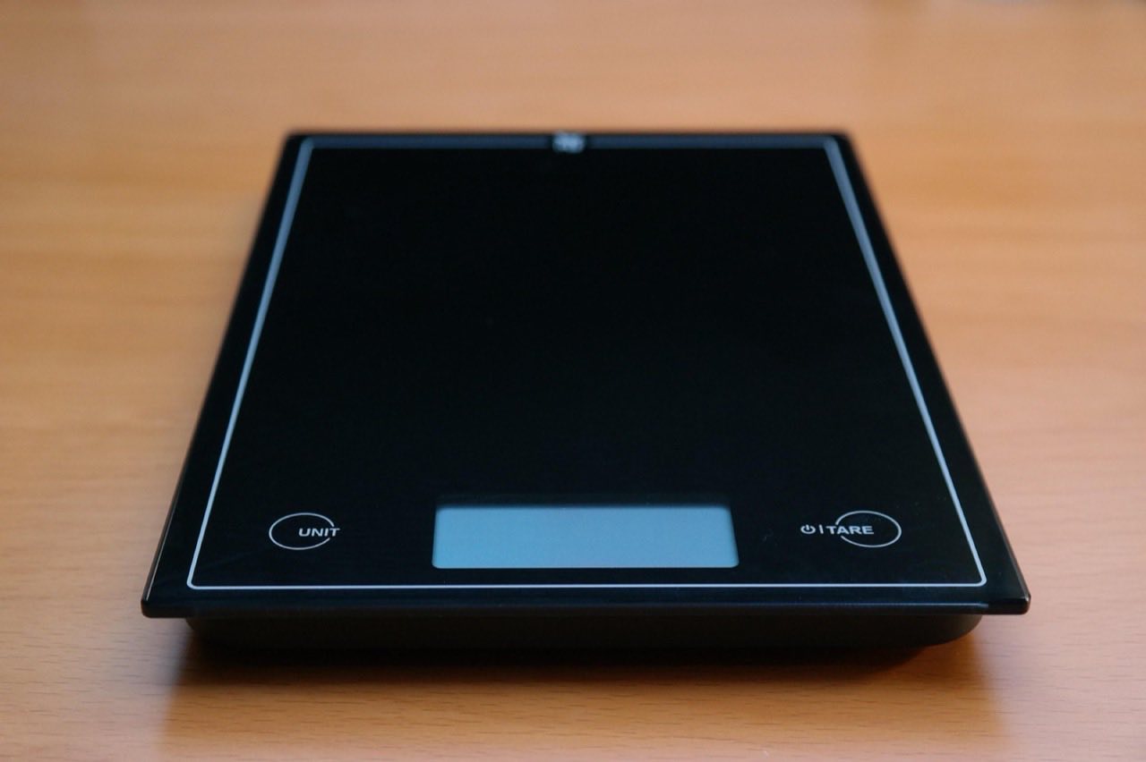 A matte black digital kitchen scale on a wood surface, its display panel dark