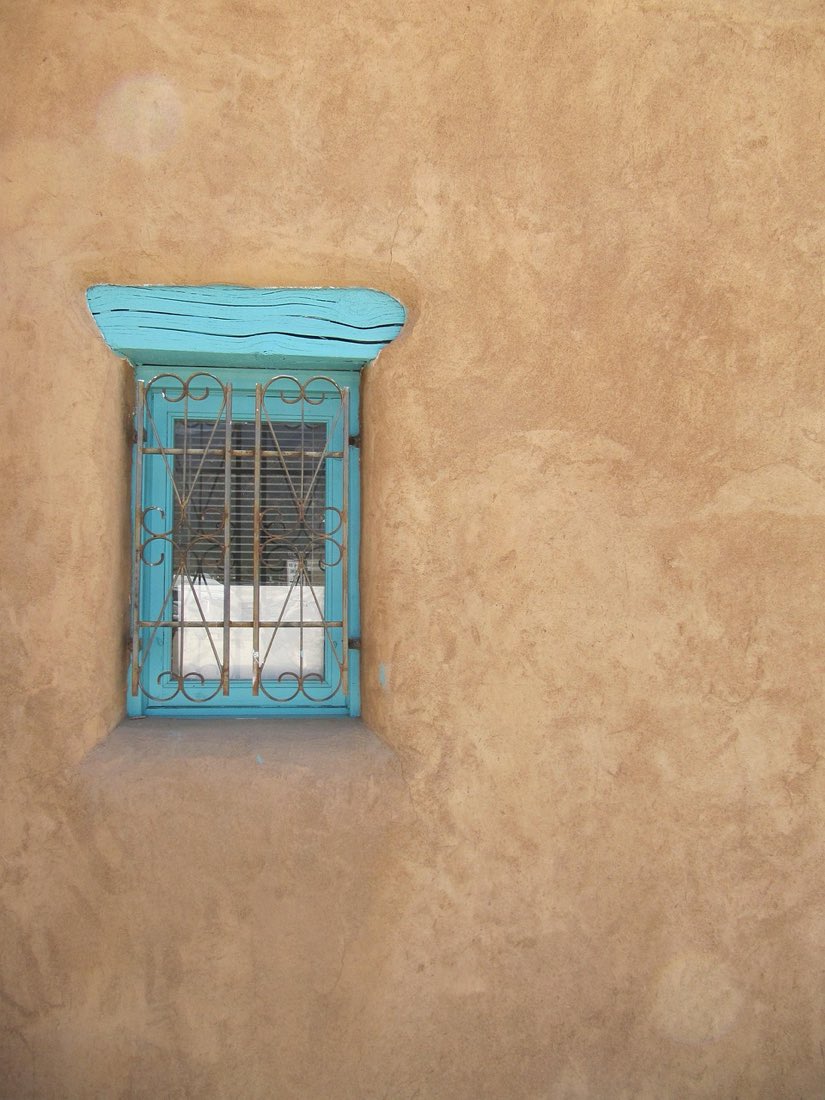 A turquoise-trimmed window set into a warm, hand-troweled lime-plaster adobe wall in Santa Fe