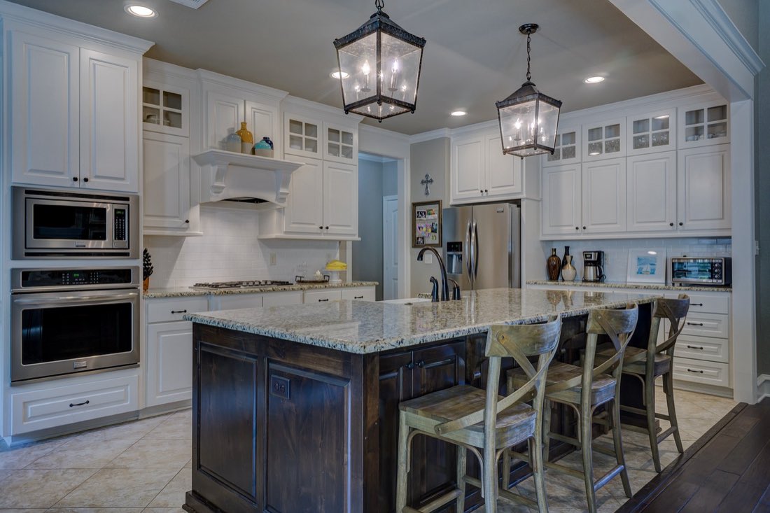 A residential kitchen mid-renovation with white cabinetry, stone countertops and pendant lighting