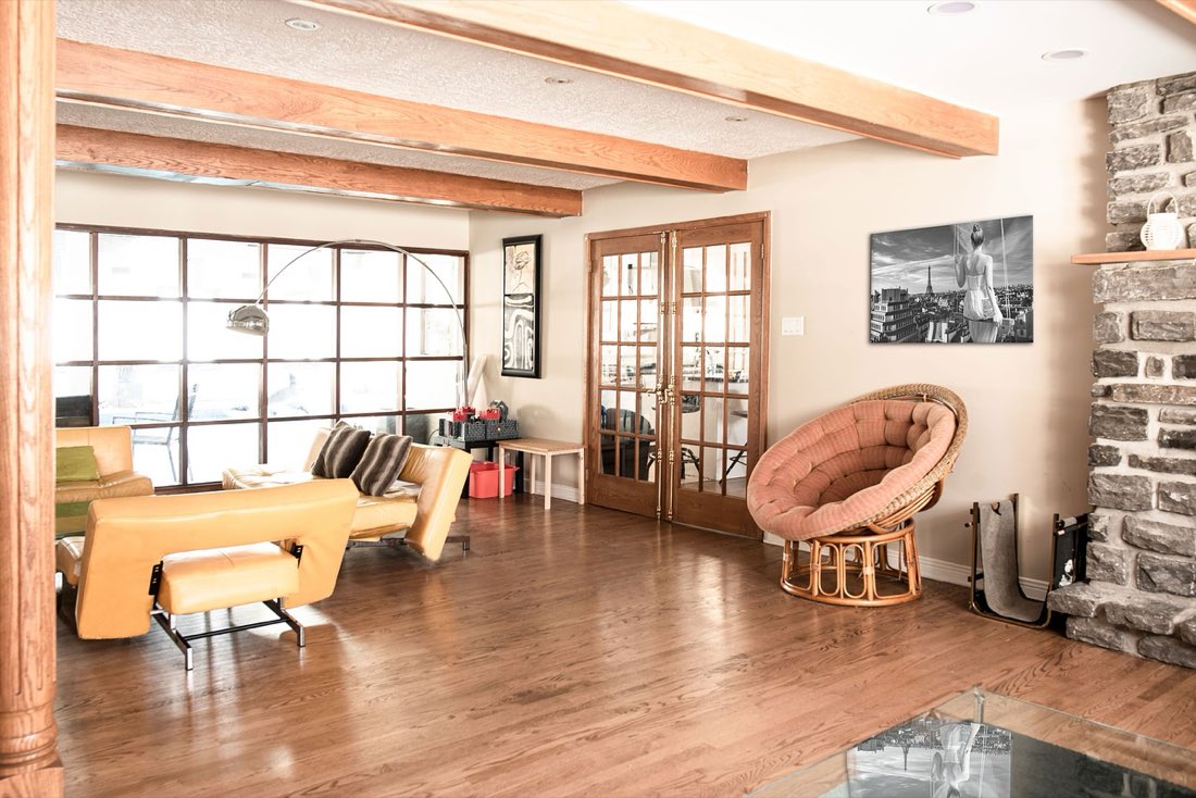 A living room with exposed wood ceiling beams, a stone fireplace and warm wood flooring